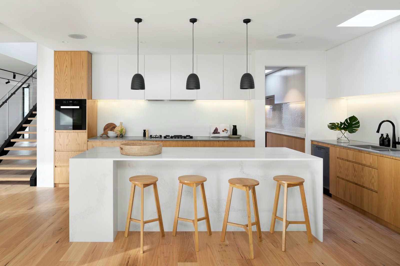 Kitchen with clear counters, a white stone island, four wooden stools and wide oak floors